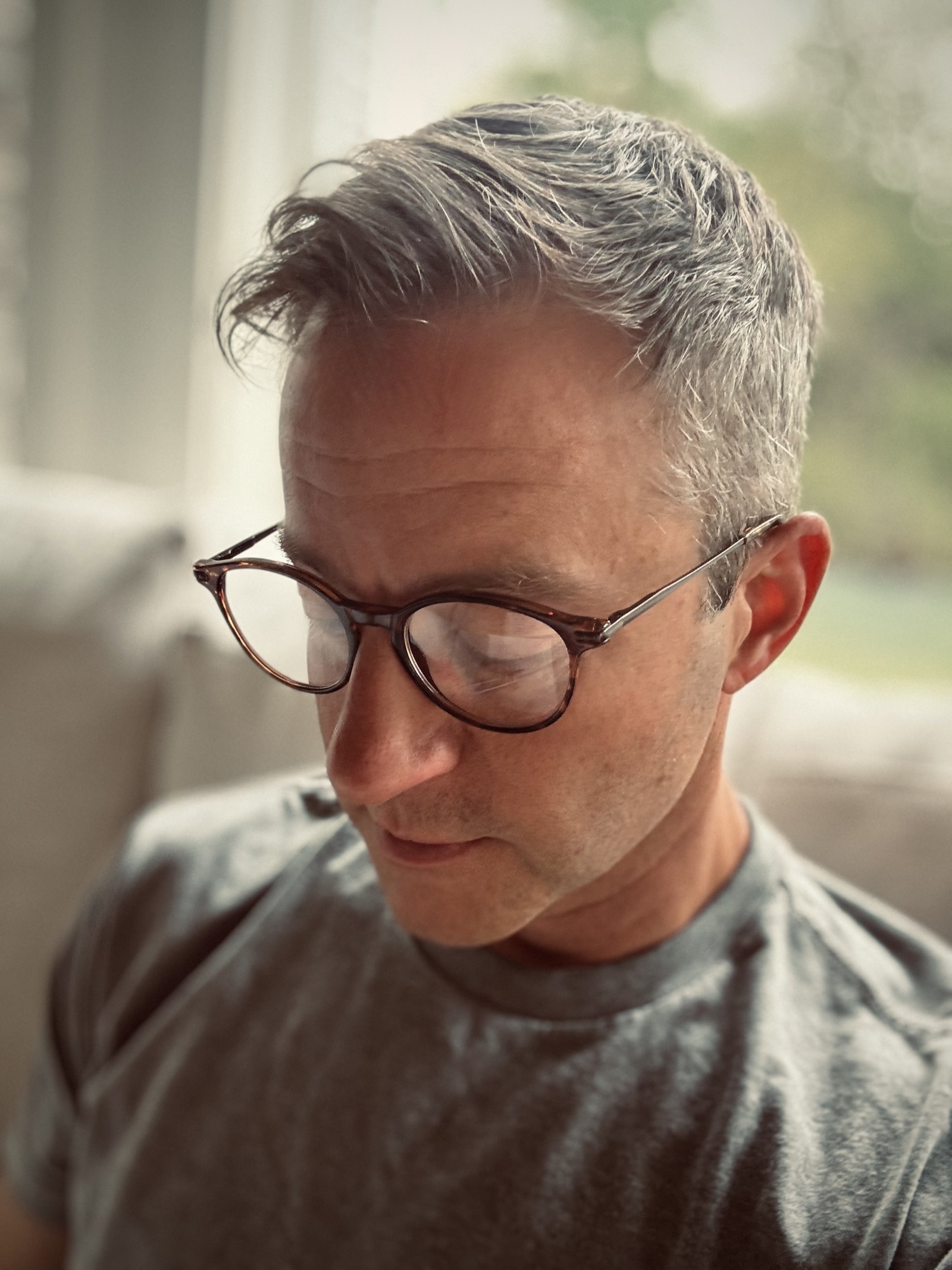 Dan Storch, looking down, wearing round tortoiseshell glasses and a grey t-shirt